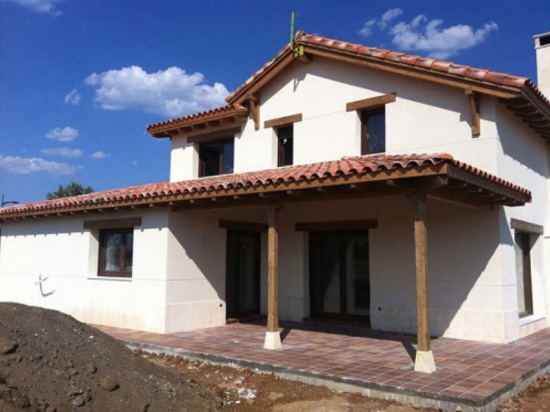 Imagen de obra nueva de chalet de dos plantas, fachada blanca y porche con vigas de madera